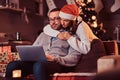 Portrait of an adorable couple - charming woman in Santa hat hugging her man and using a laptop. Royalty Free Stock Photo