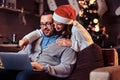 Portrait of an adorable couple - charming woman in Santa hat hugging her man and using a laptop. Royalty Free Stock Photo