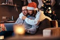 Portrait of an adorable couple - charming woman in Santa hat hugging her man and using a laptop. Royalty Free Stock Photo