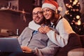 Portrait of an adorable couple with laptop - charming woman in Santa hat hugging her man and looking at camera. Royalty Free Stock Photo