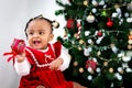 Portrait of adorable happy smiling African American little girl child holding small gift box present under Christmas tree on in Royalty Free Stock Photo