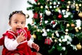 Portrait of adorable happy smiling African American little girl child holding small gift box present under Christmas tree on in Royalty Free Stock Photo