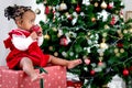 Portrait of adorable happy smiling African American little girl child sitting on big gift box present under Christmas tree in Royalty Free Stock Photo