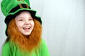 Portrait of adorable laughting seven years old girl with decorative red beard in green clothes and leprechaun\'s hat