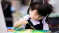 Portrait of adorable little Asian child girl holding a paintbrush and working painting on canvas for art class in classroom. Royalty Free Stock Photo
