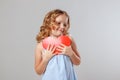 Portrait of an adorable little child girl cuddles a red paper heart. Gray background, studio