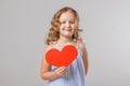 Portrait of an adorable little child girl holding a red paper heart. Gray background, studio