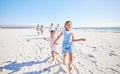 Portrait of adorable little girl and boy holding hands while running together on sandy beach while family follow in the Royalty Free Stock Photo