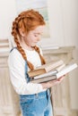 Portrait of adorable little redhead girl holding pile of books Royalty Free Stock Photo