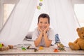 Portrait of adorable small schoolboy lying floor build camping tent fort toys wear white shirt modern interior playroom Royalty Free Stock Photo