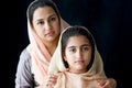 Portrait of adorable smiling Pakistani Muslim girl with beautiful eyes and her mother wearing hijab in traditional dress on dark Royalty Free Stock Photo