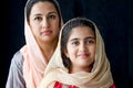 Portrait of adorable smiling Pakistani Muslim girl with beautiful eyes and her mother wearing hijab in traditional dress on dark Royalty Free Stock Photo