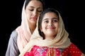 Portrait of adorable smiling Pakistani Muslim girl with beautiful eyes and her mother wearing hijab in traditional dress on dark Royalty Free Stock Photo