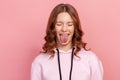 Portrait of adorable teenage girl in hoodie with eyes closed showing tongue, looking playful naughty, female millenial having fun