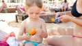 Portrait of adorable toddler boy sitting on sun bed at beach with his young mother and applying sunscreen lotion Royalty Free Stock Photo