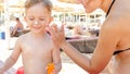 Portrait of adorable toddler boy sitting on sun bed at beach with his young mother and applying sunscreen lotion Royalty Free Stock Photo