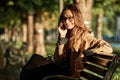 Portrait of adorable woman talking on smartphone while sitting on bench in sunlit alley