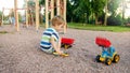 Portrait of adorable 3 years old toddler boy playing with toy truck with trailer on the playground at park. Child Royalty Free Stock Photo