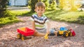 Portrait of adorable 3 years old toddler boy playing with toy truck with trailer on the playground at park. Child Royalty Free Stock Photo