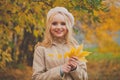 Portrait of adorable young happy blonde woman wearing french beret with autumn leaves outddor