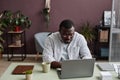 Adult black man using laptop in minimal office decorated with live green plants Royalty Free Stock Photo