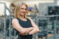 Portrait of adult blonde fitness woman personal trainer with folded hands in the gym, beautiful smiling female looking Royalty Free Stock Photo