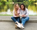 Portrait of Adult caucasian daughter showing on mobile phone to her senior mother outdoor in summer park, near lake Royalty Free Stock Photo