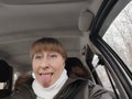 Portrait of adult cute funny blonde woman in warm clothes taking a selfie inside the car and driving it. The concept of