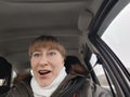 Portrait of adult cute funny blonde woman in warm clothes taking a selfie inside the car and driving it. The concept of