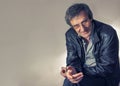 Portrait of an adult gray-haired man in glasses sitting with a questioning look on a chair in a light gray shirt and Royalty Free Stock Photo