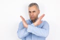 Portrait of adult handsome man with grey hair wearing blue shirt showing no sign by crossing his hands standing on  white Royalty Free Stock Photo