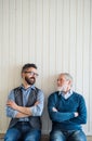 A portrait of adult hipster son and senior father sitting on floor indoors at home.