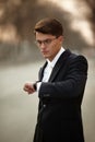 Portrait of an adult male model with glasses. Business man wearing black suit and white tie, looking at the his watch. Royalty Free Stock Photo