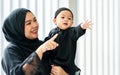 Portrait Adult muslim mother wearing traditional black dress and headscarf, carrying little baby boy, smiling with happiness in Royalty Free Stock Photo