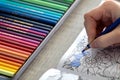 A portrait of an adult person coloring in a coloring book for adults with a blue colored pencil in their hand. There is also a