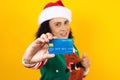 Portrait of adult woman holding a credit card for shopping at Christmas wearing a santa hat on yellow background in Mexico latin A Royalty Free Stock Photo