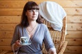 Portrait of an adult woman wearing gray bathrobe holding a cup of coffee, one person sitting rattan chair at home