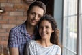 Portrait of affectionate young spouses standing at home by window