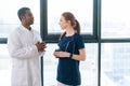 Portrait of African American black male doctor in white coat talking with positive redhead young nurse wearing blue Royalty Free Stock Photo