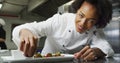 Portrait of african american female chef garnishing dish looking at camera and similing