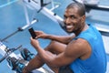 Fit man using mobile phone while exercising on rowing machine in fitness center Royalty Free Stock Photo