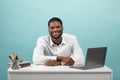 Portrait of african american freelancer man sitting at desk with laptop, smiling at camera over blue background Royalty Free Stock Photo