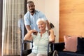 Portrait of african american male health worker and caucasian senior woman on wheelchair at home