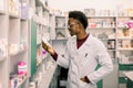 Portrait of African American male pharmacist standing in interior of pharmacy and looking at the medicine in hand Royalty Free Stock Photo