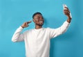 Portrait of an African-American man taking a selfie and smiling on a blue isolated background Royalty Free Stock Photo