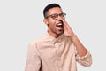 Portrait of African American man wearing round eyewear, beige shirt, screaming with wide opened mouth. Furious dark-skinned male Royalty Free Stock Photo