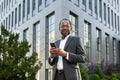 Portrait of African American mature businessman, senior man outside office building holding phone in hands smiling and Royalty Free Stock Photo