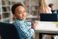 Portrait of african american schoolboy sitting at desk in classroom, turning back and smiling at camera, free space