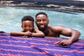 Portrait of african american shirtless father and son leaning at poolside in tourist resort