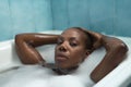 Portrait of African American woman, with her hands on her head and taking a bath with the bathtub full of foam, very relaxed.